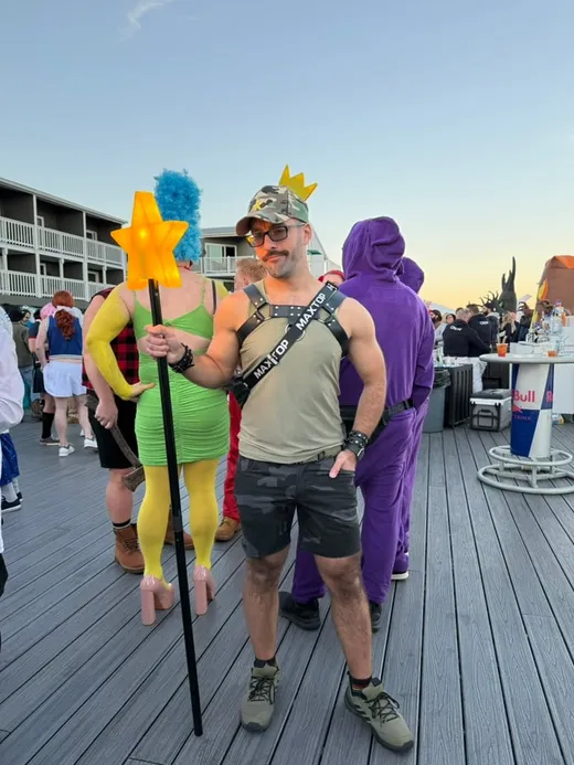 Salem on the Boatslip deck at sunset in camo shorts and a harness, holding a glowing star wand